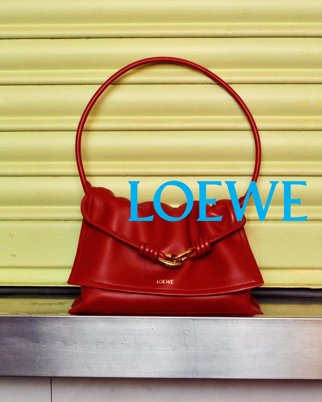 Red leather handbag with a circular handle placed against a light yellow ridged surface