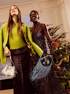 Grace Elizabeth and Awar Odhiang in Tory Burch Holiday 2026 campaign, wearing neon green jacket and embellished dress with designer handbags.
