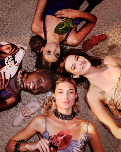 Four female models lying in a circle with their heads together on an animal print rug, holding sandals for Tory Burch.
