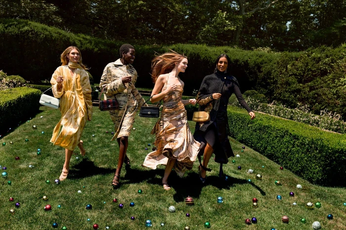 Four female models running across a lawn scattered with small ornaments during a Tory Burch campaign.