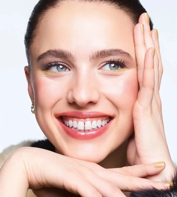 Close-up portrait of Margaret Qualley smiling with gold eyeliner and gold nail polish for Chanel Holiday 2026