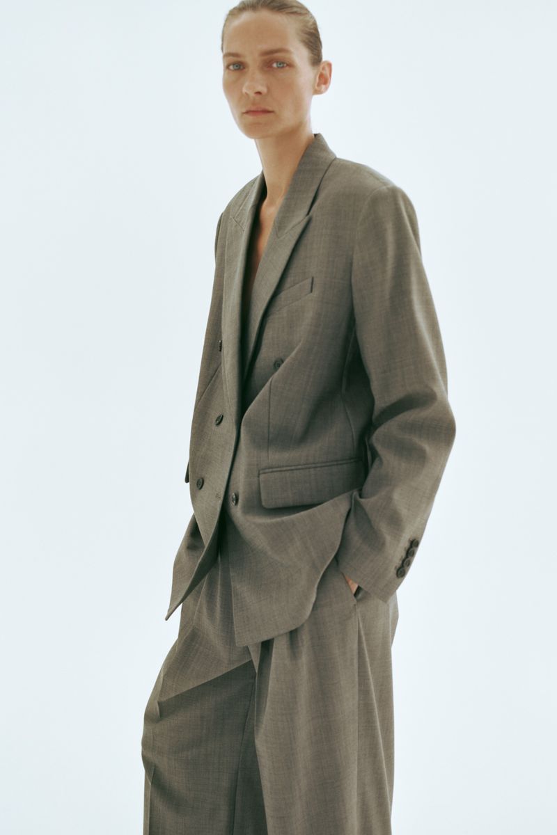 Model Karolin Wolter wearing a grey tailored double-breasted blazer and trousers against a bright white background for H&M.