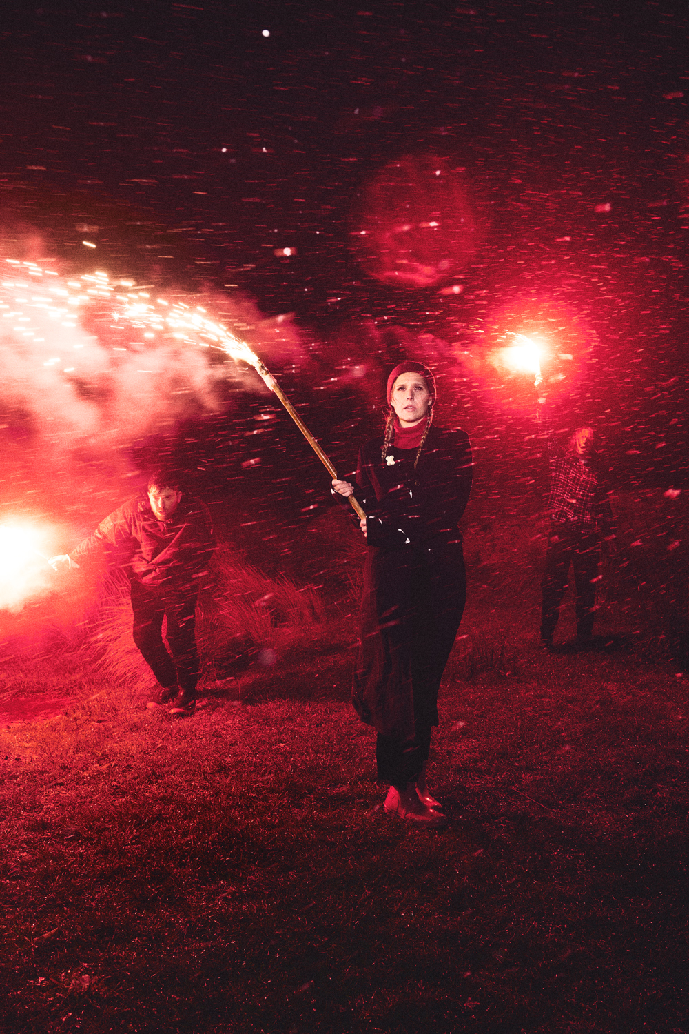 A woman stands holding a sparkler stick as other people walk in a field at night with their own sparklers, celebrating.