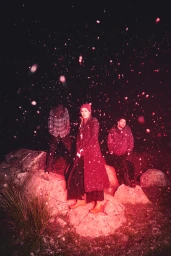 Three people outdoors at night under red lighting amid falling snow, captured by photographer Seiya Taguchi for The Middle Kids.