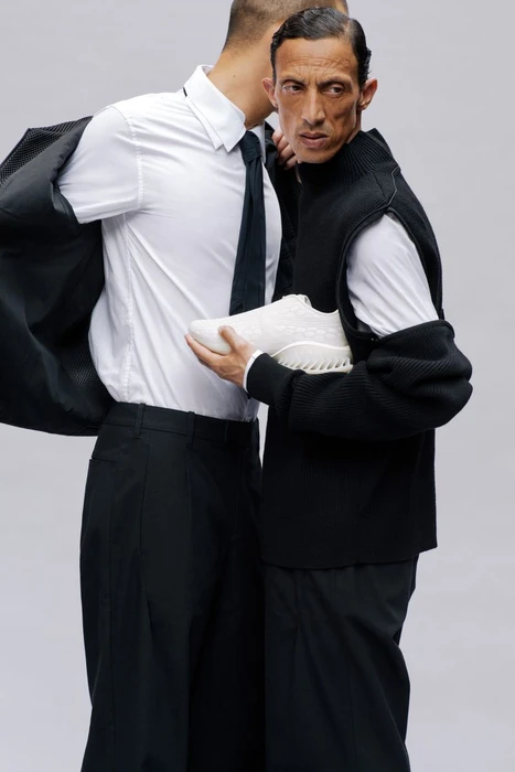 Two men posing closely together holding a white sneaker against a plain grey backdrop for Puma