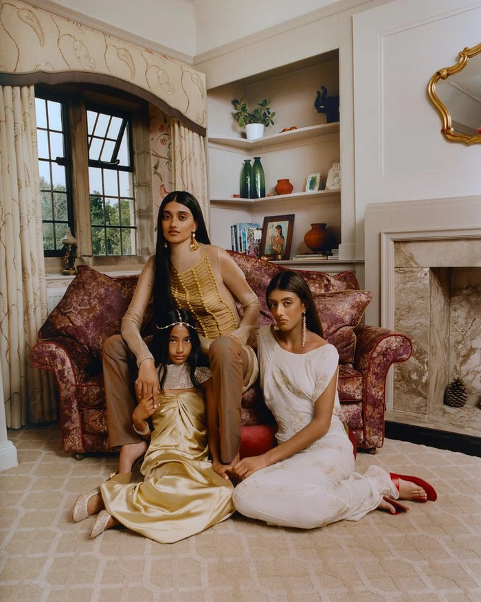 Three models posed elegantly together on a patterned sofa in a traditional living room for British Vogue Divine Diwali editorial