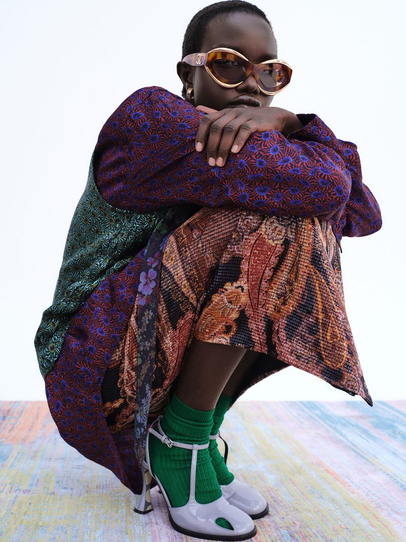 Model Akon Changkou wearing oversized sunglasses and patterned clothing crouches against a plain backdrop.