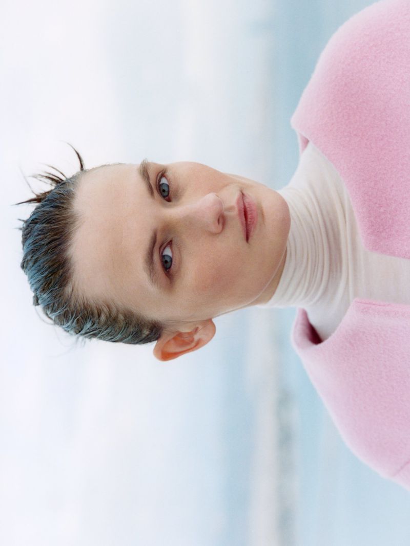 Model Lara Mullen wearing a pink coat and white turtleneck against a bright overcast sky for Vogue Greece urban armor editorial