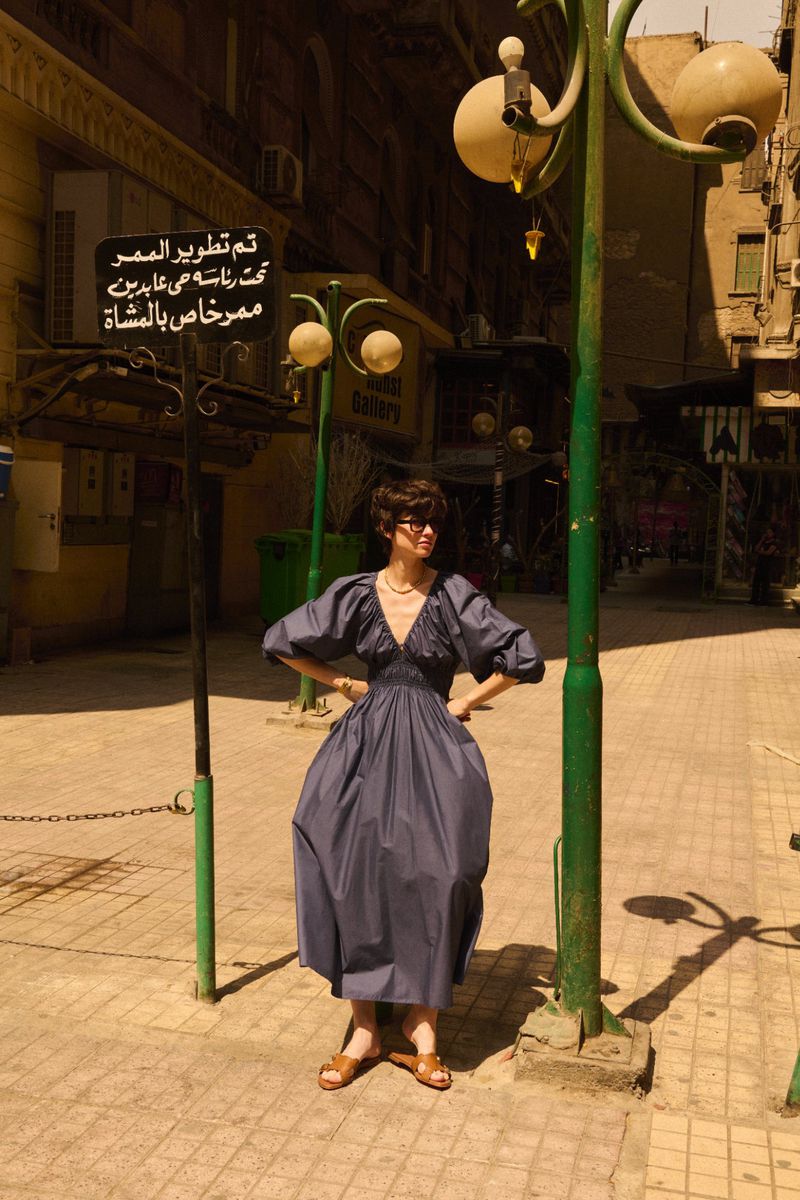 Woman poses in a blue dress on a city street in Egypt. The vintage street lamp and Arabic signage add to the scene's cultural backdrop.