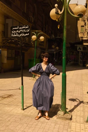 Woman poses in a blue dress on a city street in Egypt. The vintage street lamp and Arabic signage add to the scene's cultural backdrop.