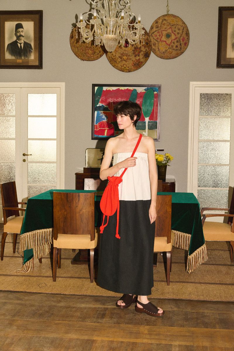 A woman in a white strapless top and black skirt stands in a room with a table, chairs, and artwork in a light-filled interior.