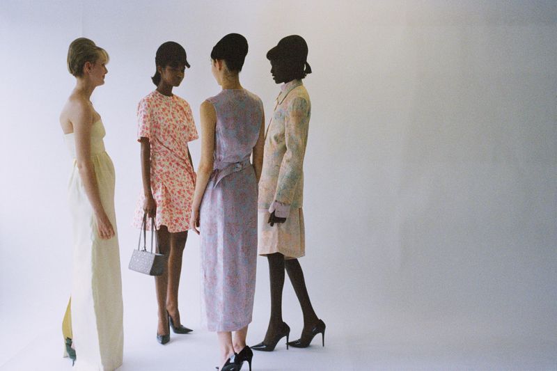 Four models wearing pastel dresses, retro caps, and high heels standing together against a bright white seamless background.