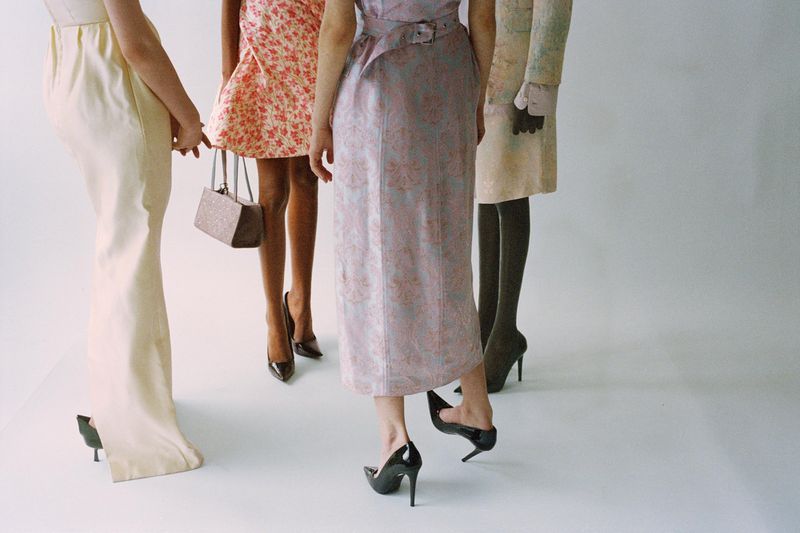 Four women in fashionable dresses and high heels, studio shot, showcasing a range of styles from floral to pastel, elegant, and chic.