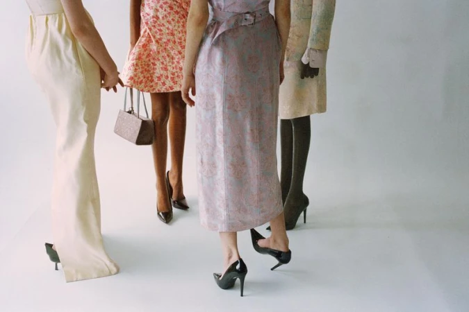 Four women in fashionable dresses and high heels, studio shot, showcasing a range of styles from floral to pastel, elegant, and chic.