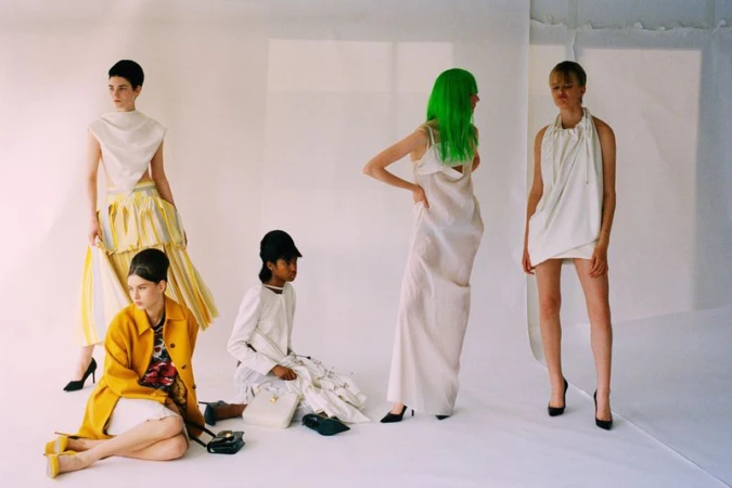 Five female models in avant-garde white and yellow outfits with one model sporting bright green hair in a white studio setting.