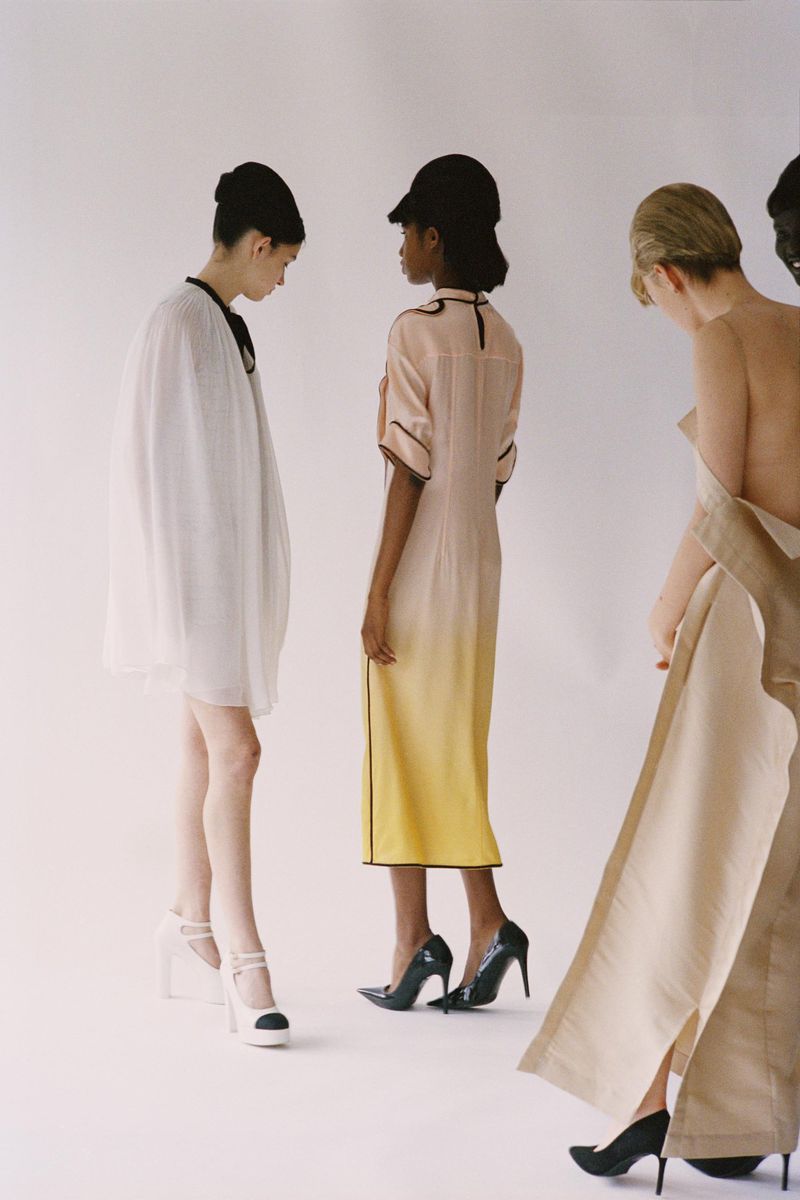 Group of fashion models in dresses and high heels posing in front of a plain white backdrop in a fashion studio setting.