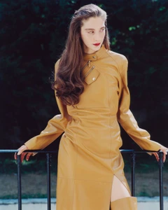 Model in amber leather jacket leaning against a dark metal railing outdoors