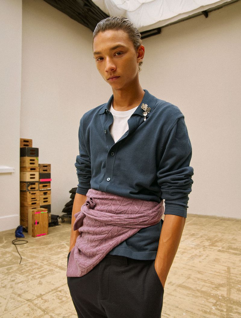 Model Charlie Tilling-Cole wearing a blue polo and pink knit sweater tied around the waist in a studio setting for Family Style.