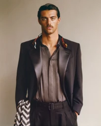 Thomas Ceccon wearing a black tailored blazer, silk shirt, and swimming goggles around his neck against a neutral studio backdrop.