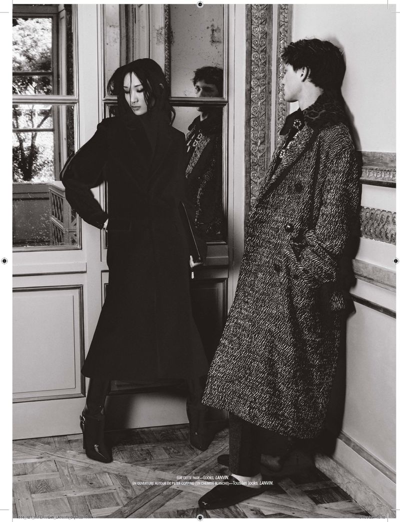 Black and white editorial fashion portrait of two models wearing textured coats in an ornate interior setting.