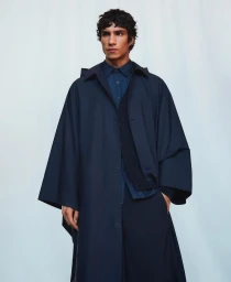 Model Duncan Yair wears an oversized navy blue cape coat over a button-up shirt in an Adolfo Domínguez studio portrait.