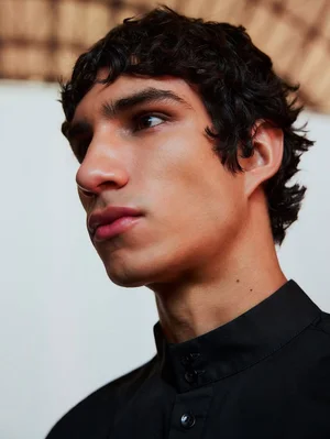 Close-up portrait of model Duncan Yair wearing a black mandarin collar shirt for Adolfo Domínguez F/W 2025.