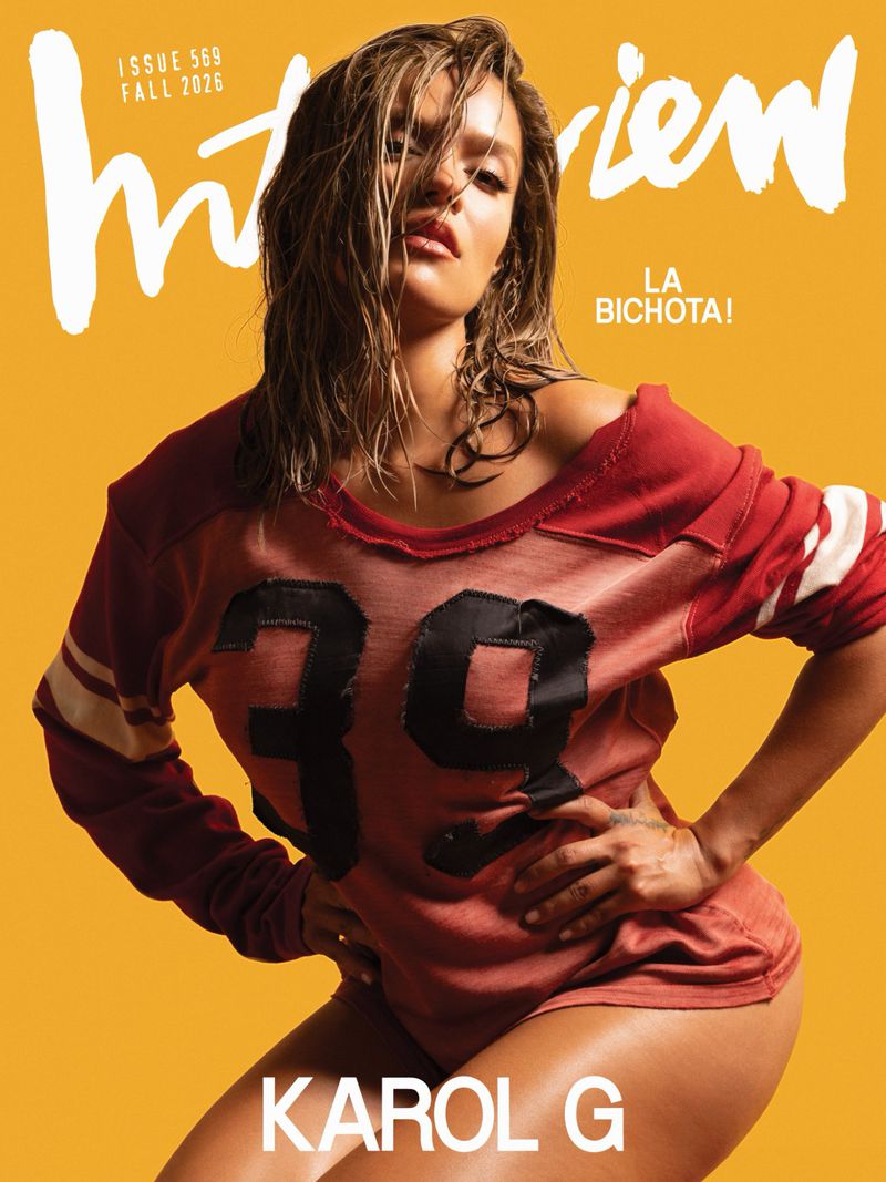 Karol G on the cover of Interview Magazine Fall 2026, wearing a red jersey against a solid yellow background.
