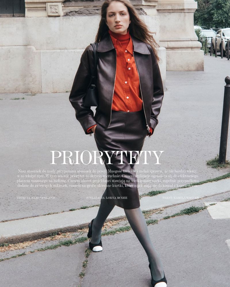 Model in brown leather jacket and skirt with orange top walking on a city street for Vogue Polska.
