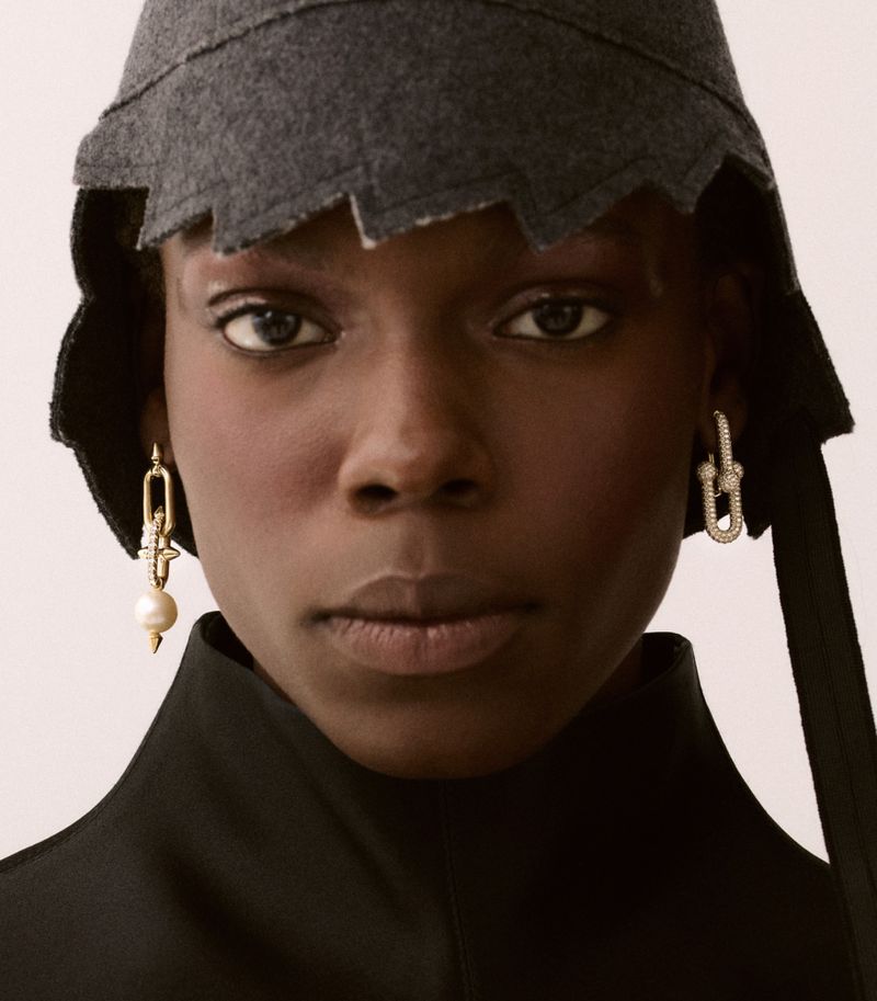 Close-up portrait of model Agel Akol wearing a dark structured hat and statement earrings for Heroine Magazine.