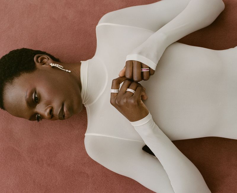Model wearing a white turtleneck and rings lying down on a textured surface