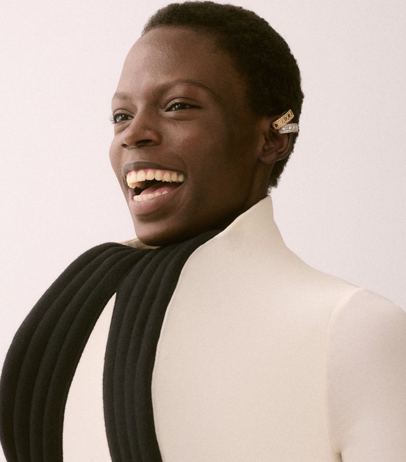 Model Agel Akol smiling wearing gold and silver ear cuffs and a structured white top with black tubular accents
