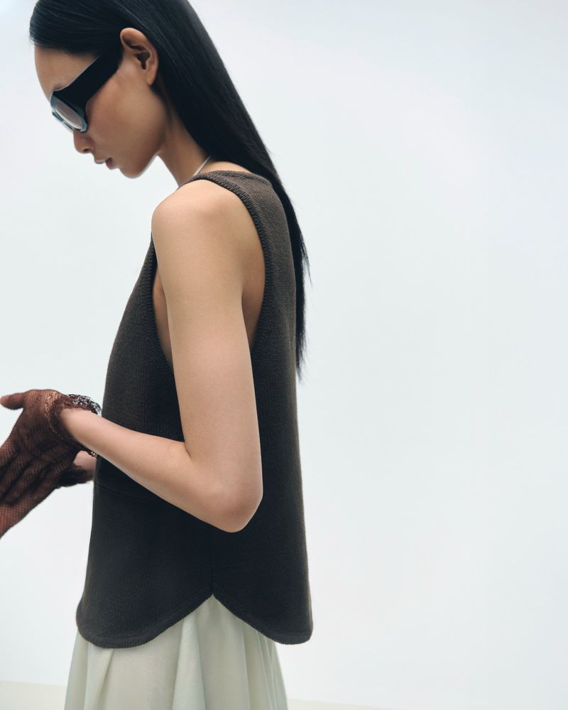 Portrait of a young Asian woman in a brown sleeveless top and light skirt, wearing sunglasses, posing in a white studio setting.
