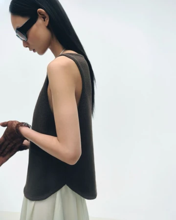 Portrait of a young Asian woman in a brown sleeveless top and light skirt, wearing sunglasses, posing in a white studio setting.