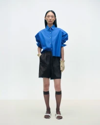 Model Ling Chen wearing an oversized cobalt blue short-sleeve shirt and black shorts against a clean white studio background.