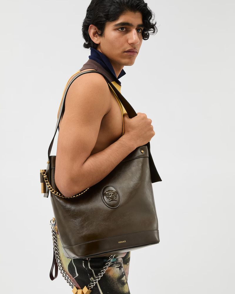 Model carrying a dark brown leather shoulder bag with gold hardware against a clean white background