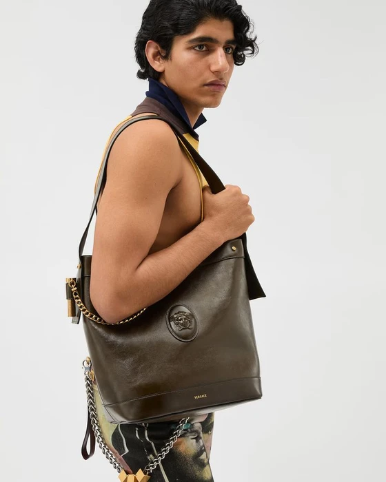 Model carrying a dark brown leather shoulder bag with gold hardware against a clean white background