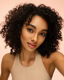Close-up portrait of a woman with dark curly hair wearing a beige top against a neutral background for Maybelline