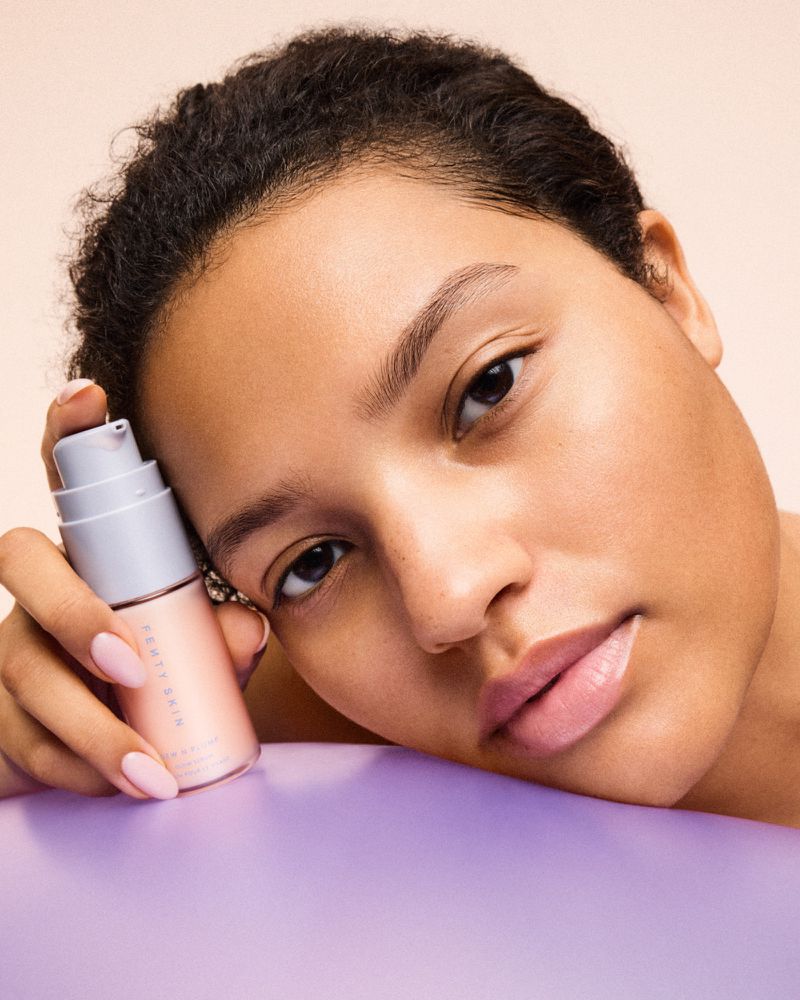 Adult female posing with Fenty Skin Start'r Set product. Light skin, light pink nails, soft focus, studio lighting, cosmetic skincare.
