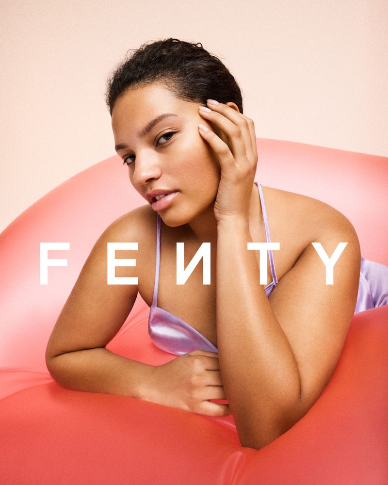 Elegant young woman in lavender silk lingerie, reclining on an inflatable coral sofa against a warm beige backdrop in a beauty editorial.