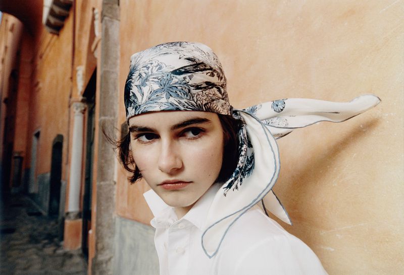 Portrait of a young woman wearing a patterned headscarf, a white blouse, with an alleyway background. Fashion and portrait photography.