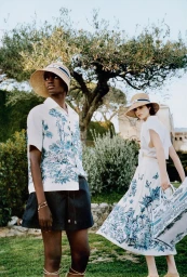 Two models wearing printed resort wear and straw hats outdoors under a tree for Dior Riviera campaign