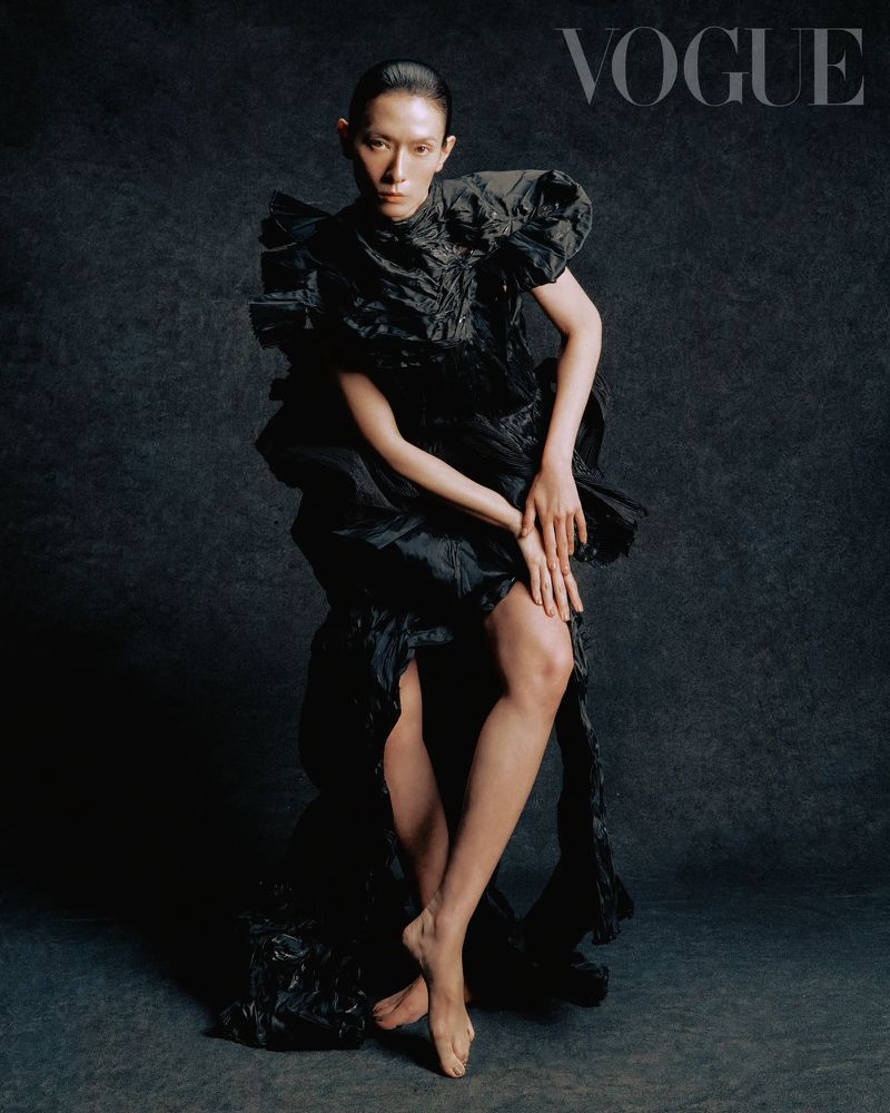 A striking fashion portrait shows an Asian adult female in a black ruffled dress, shot in a photo studio setting with dark, moody lighting.