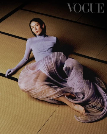 Elegant woman in a light purple outfit poses on a tatami mat for a fashion editorial, highlighted by soft lighting and a Vogue logo.