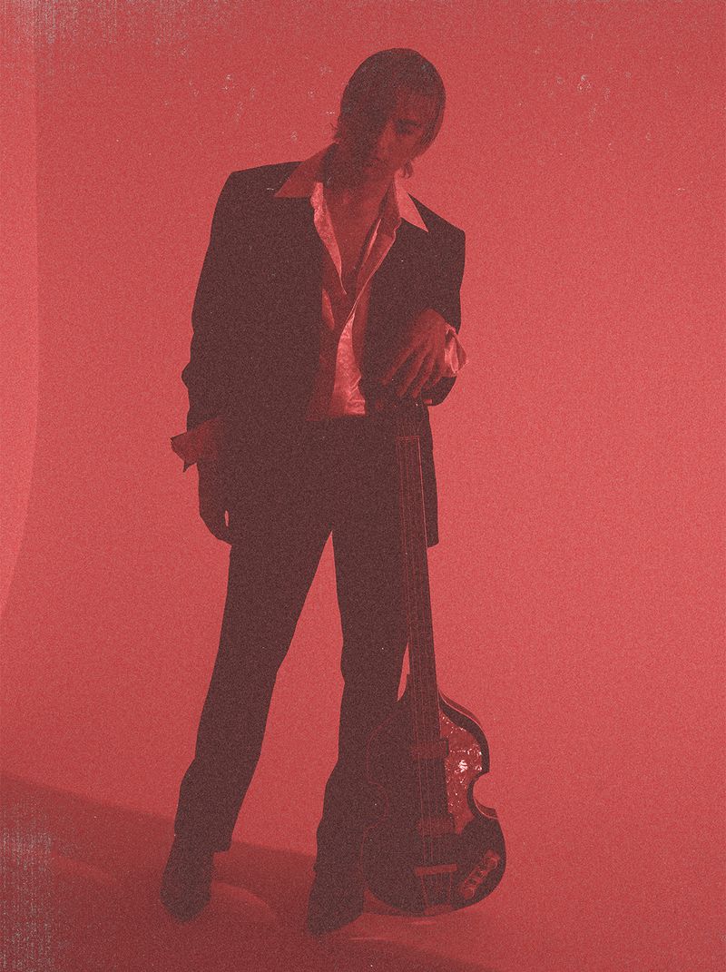Man in suit poses with bass guitar in vibrant red lighting, creating a striking musical portrait. Fashion and music collide.