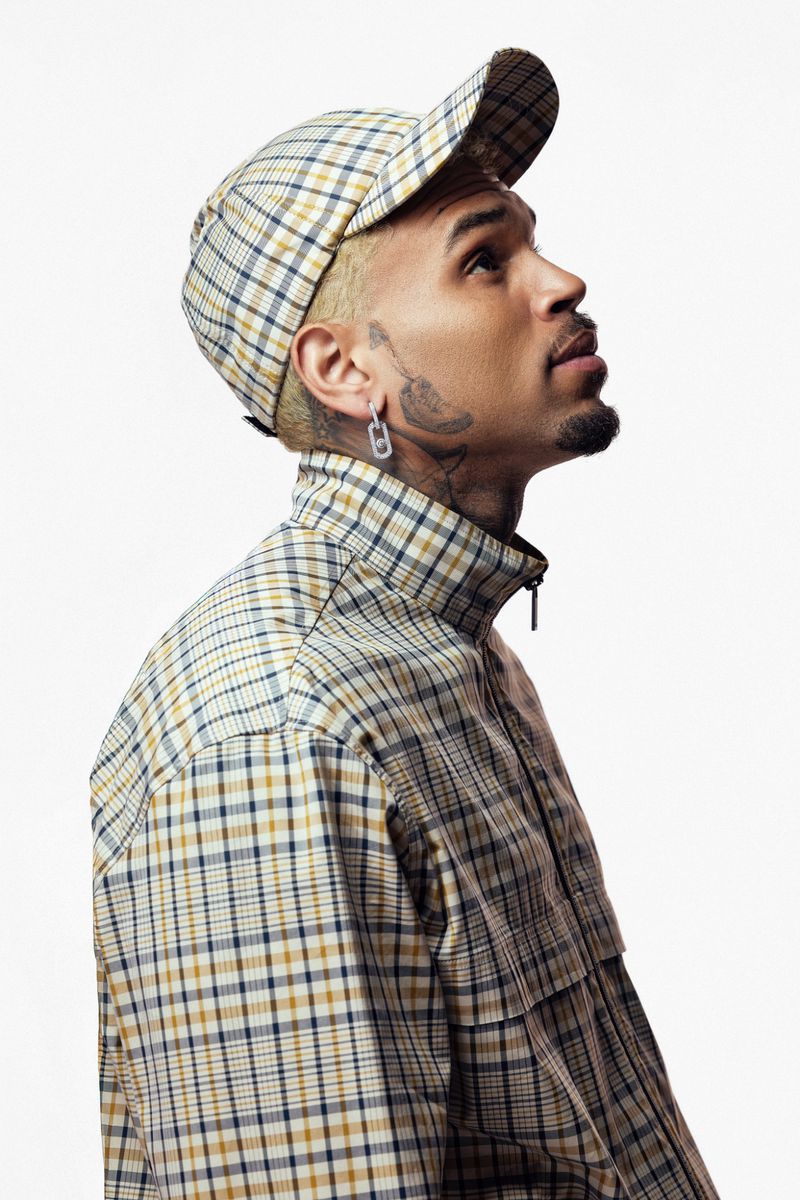Profile portrait of a man with light brown hair, wearing a plaid jacket and hat, looking up against a white background. 