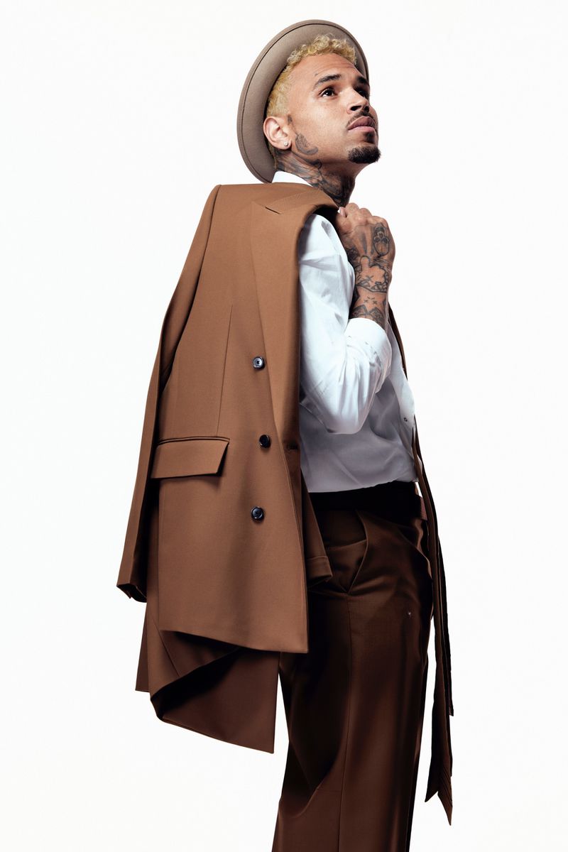 Adult male in a brown suit and hat looking upward. The subject is in a photo studio, with the coat draped over his shoulder.