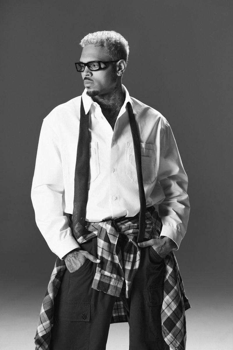 Black and white portrait of an adult male wearing glasses, shirt, and tie, with a plaid shirt around his waist, against a gray background.