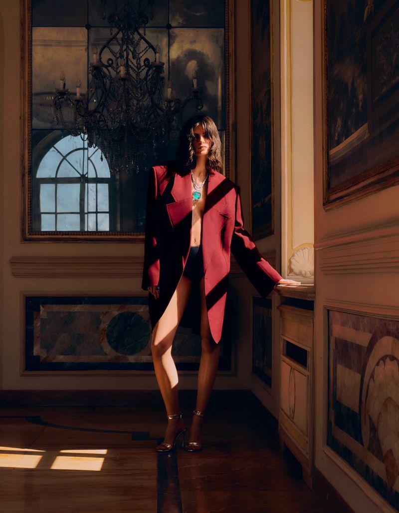 Fashionable woman poses in an oversized marsala jacket and heels, showcasing turquoise jewelry in an elegant interior setting.