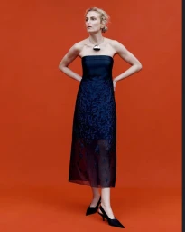Model in strapless dark blue midi dress wearing statement necklace against a vibrant red backdrop