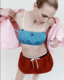 Model wearing a blue bandeau top and red shorts with a pink jacket pulled back against a plain white studio background.